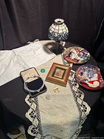Overall lot on table showing lamp, linens, plates, framed print, jewelry case