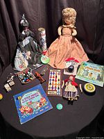 Overview of all items on black round table: dolls, kaleidoscope, yo-yo, puck, marbles, game, miniature furniture, car, Disney book & record sets