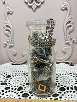 Bottle filled with assorted silver-tone jewelry pieces
