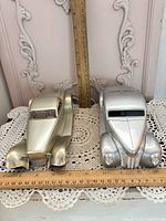 Both silver die-cast model cars side by side with rulers for scale