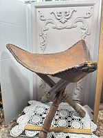 Full view of folding stool showing leather seat and wood frame