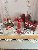 Wide view of all shakers, stands and peanut figurine on lace cloth