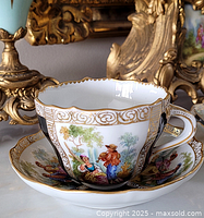 cup resting on saucer showing painted scene, gilt trim, and black panels