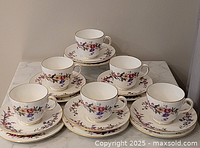Five of the six tea trios displayed: cups on saucers with dessert plates beneath