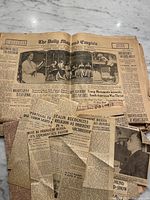 Open newspaper with visible masthead and loose clippings surrounding it