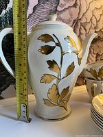 coffee pot with measuring tape showing height and gold leaf design