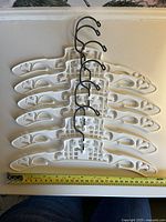 All six white plastic baby hangers stacked, measuring tape showing 12 in width