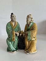 Front view of two seated mudmen sharing tea on black base