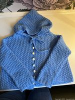 Front view of blue hand-knit hooded sweater showing buttons and tie