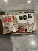 Loose stamps in plastic box showing various designs and denominations