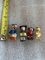 Front view of four miniature Disney figurines with tape measure showing scale
