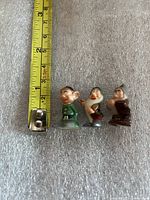Three dwarf figurines beside tape for scale