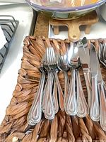 Flatware assortment on woven tray showing forks, spoons, knives with beaded handles