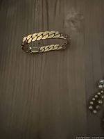 Gold-filled Cuban link hinged bangle bracelet closed on tabletop