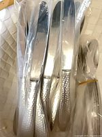 Group of five dinner knives in sleeves and bundled spoons showing hammered handles