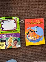 Front covers of both books showing Disney Aladdin storybook and Disney Fairies Magical Drawings with magnetic board