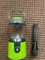 Green Woods lantern beside black Hyundai flashlight