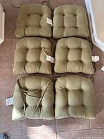 Six olive-green tufted seat cushions laid out showing tops and ties