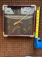 Front view of Deko square wall clock beside tape for scale