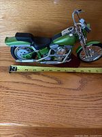 Left side view of green Harley-Davidson model motorcycle on stand with tape measure showing length