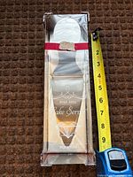 Front view of boxed high heel cake server with measuring tape indicating size