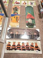 Overview of five shrink-wrapped Anne Geddes prints on floor: two horizontal (bee babies, hanging cocoons) and three vertical (cactus pot, toadstool, additional print)