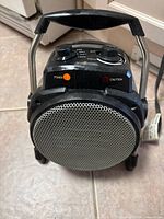 Front view of barrel-style electric space heater showing grille, LED indicators, knobs and carry handle