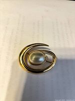 Front view of gold-tone swirl brooch with faux pearl center