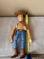 Front view of Woody doll next to tape showing height