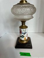 Full view of oil lamp showing glass font, ceramic column, brass fittings, wood base