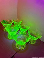 Six uranium glass pedestal dessert cups glowing under UV light