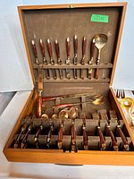 Overall view of open wooden flatware box showing knives in lid, forks, spoons and serving pieces in base