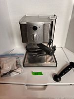 Front view of Breville espresso machine with portafilter attached, accessory bag and scoop-tamper visible