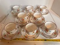 Full set of eight cups with saucers laid out, ruler for scale