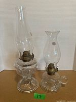 Both clear glass oil lamps standing side by side showing overall design