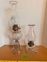 Two clear glass oil lamps with chimneys side by side