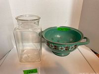 Square clear glass apothecary-style jar and green enamel floral colander side by side