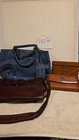 Group shot showing blue tote, brown braided-strap handbag, two tan wallets