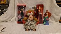 Group shot showing both boxed Barbie dolls, plush bear holding baby doll, and Ariel figure