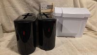 Two black towel dispensers and white receptacle side by side