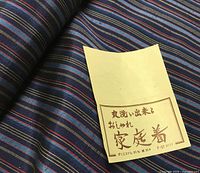 Close-up of fabric showing dark blue ground and narrow multicolor stripes with attached Japanese tag