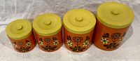 Front view of four graduated orange floral lacquer canisters with yellow lids