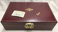 Closed burgundy leather jewellery box with key and product tag on lid