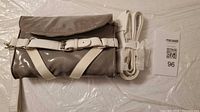 Front view showing gray patent body, white buckle strap, white cross webbing, curved flap