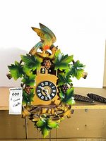Front view of carved and painted wood cuckoo clock with bird, leaves, dial, chains and weights