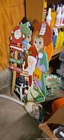 Group of painted wooden yard stakes leaning against shelf, showing Santa figures, scarecrow, gnome, pumpkin