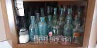 Shelf with majority of aqua bottles, clear jar, row of small clear bottles