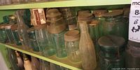 Shelved assortment of aqua and clear canning jars with varied lids, plus one clear bottle