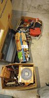 overview of three open boxes containing metal toolbox, packaged tools, leather pouch and various hand tools