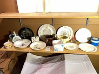 Shelf view showing assorted plates, bowls, mugs, cachepot, tissue box cover, brass swans, glassware
